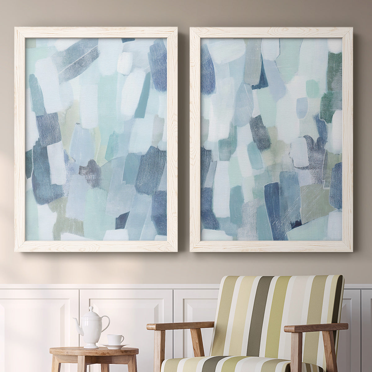 Set of two white barnwood framed canvas prints depicting two cool-toned geometric abstracts featuring fragmented pale blue green gray and white brush blocks above a sideboard in a cozy sitting room.