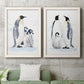 Set of two white barnwood framed canvas prints depicting a coordinated art pair of adult emperor penguins with fluffy chicks rendered as soft watercolor wildlife illustrations above a sofa in a modern living room.