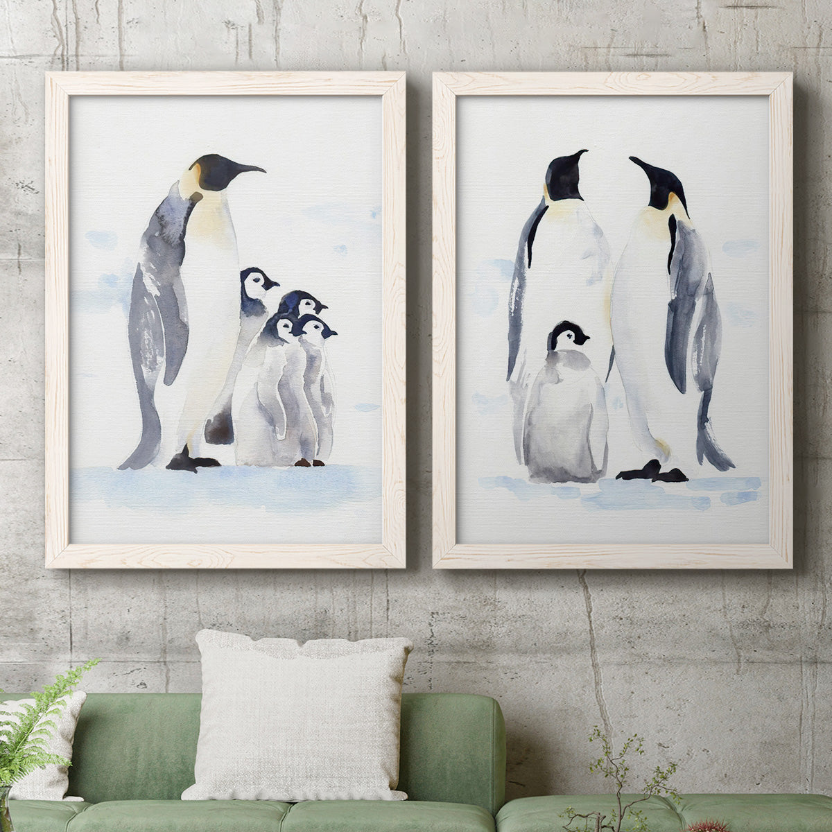 Set of two white barnwood framed canvas prints depicting a coordinated art pair of adult emperor penguins with fluffy chicks rendered as soft watercolor wildlife illustrations above a sofa in a modern living room.
