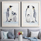 Set of two white barnwood framed canvas prints depicting paired soft watercolor wildlife illustrations with black white and yellow birds standing on pale icy ground above a sofa in a contemporary living room.