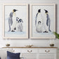 Set of two white barnwood framed canvas prints depicting a coordinated art pair of adult emperor penguins with fluffy chicks rendered as soft watercolor wildlife illustrations above a dining room sideboard.
