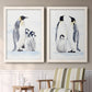 Set of two white barnwood framed canvas prints depicting two soft watercolor wildlife illustrations featuring adult emperor penguins with fluffy chicks above a sideboard in a cozy sitting room.