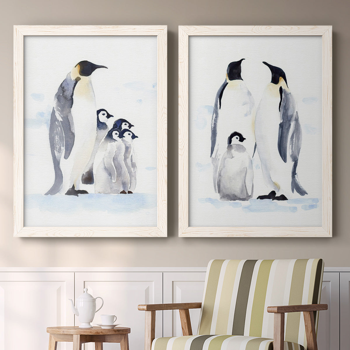Set of two white barnwood framed canvas prints depicting two soft watercolor wildlife illustrations featuring adult emperor penguins with fluffy chicks above a sideboard in a cozy sitting room.