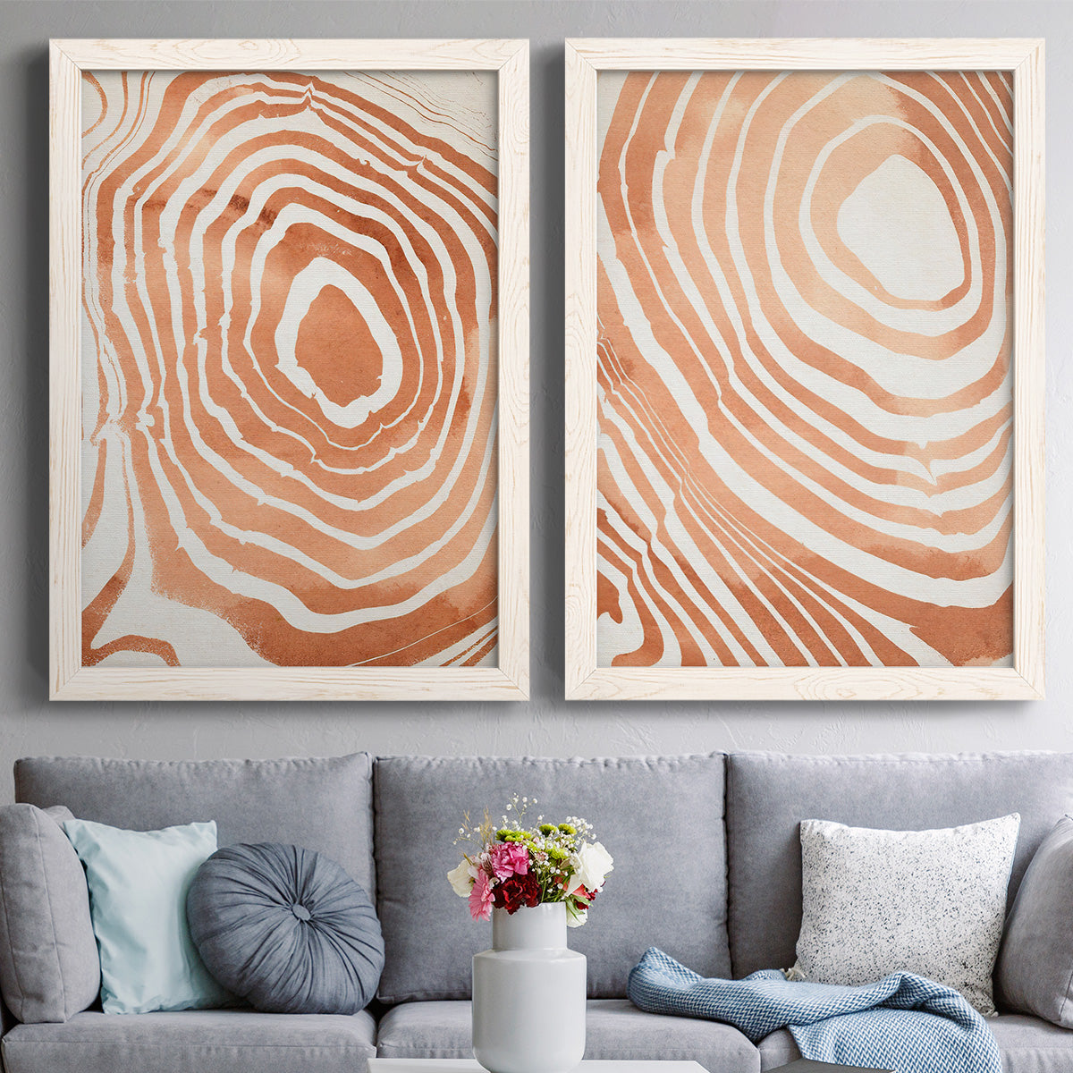 Set of two white barnwood framed canvas prints depicting paired minimalist marbled pattern abstracts with warm terracotta lines, cream negative space, and organic nested curves above a sofa in a contemporary living room.