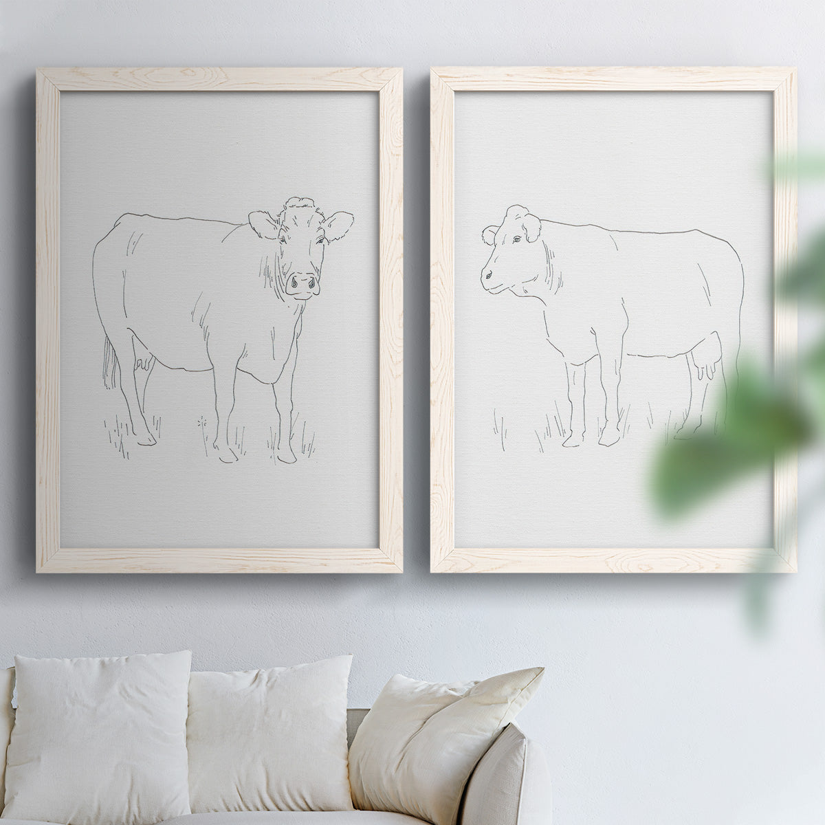 Set of two white barnwood framed canvas prints depicting fine gray lines, white backgrounds, and quiet farm-animal profiles arranged across two complementary compositions above a sofa in a bright living space.