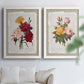 Set of two white barnwood framed canvas prints depicting roses anemones carnations leaves and archival script details arranged across two complementary compositions above a sofa in a bright living space.