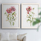 Set of two white barnwood framed canvas prints depicting fine green stems, open rose petals, and ample white space arranged across two complementary compositions above a sofa in a bright living space.