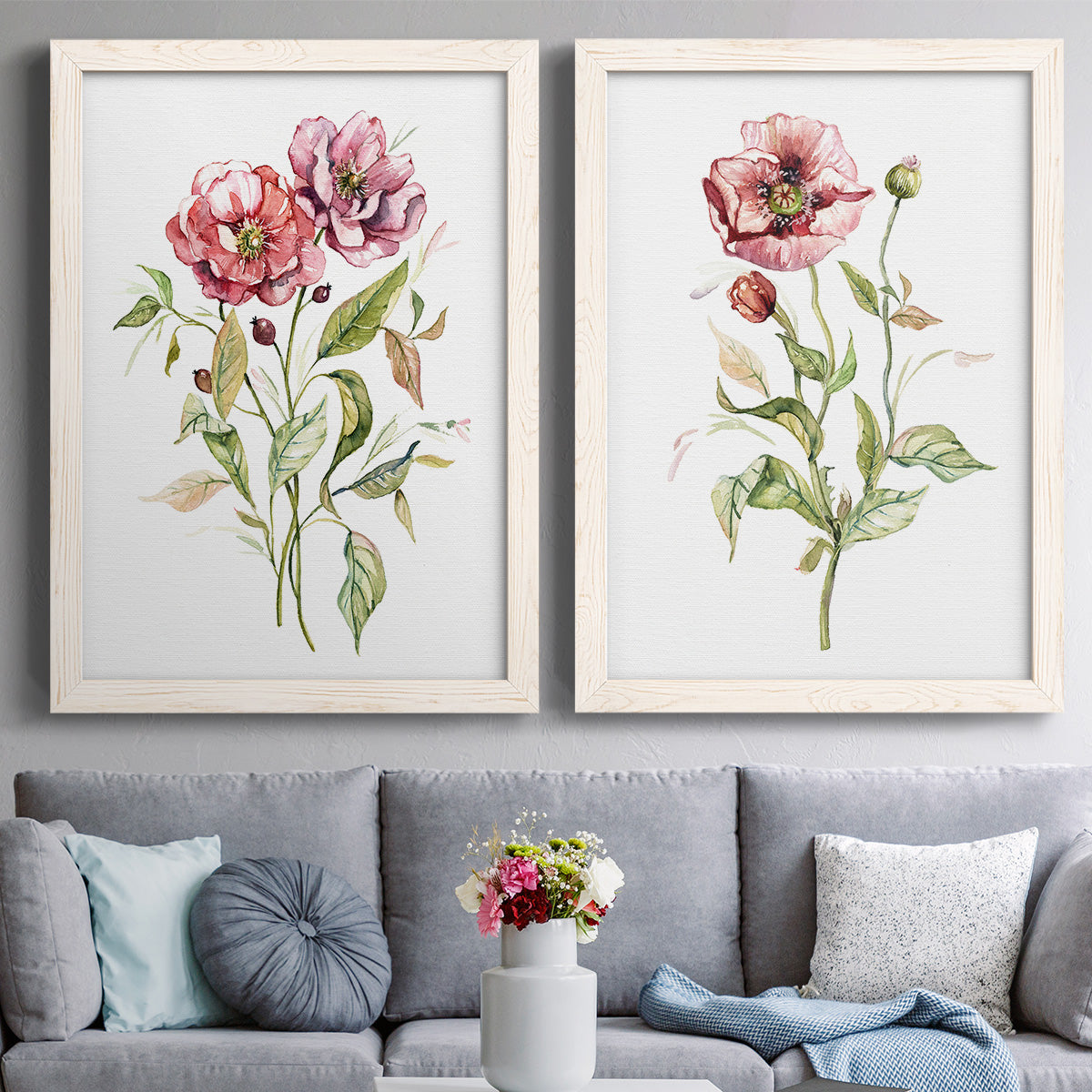 Set of two white barnwood framed canvas prints depicting paired traditional watercolor flower studies with fine green stems, open rose petals, and ample white space above a sofa in a contemporary living room.