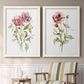 Set of two white barnwood framed canvas prints depicting two traditional watercolor flower studies featuring two airy wildflower stems with pink and burgundy blossoms above a sideboard in a cozy sitting room.