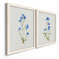 Angled view of a set of two white barnwood framed canvas prints featuring two delicate watercolor botanical studies featuring small blue wildflower stems.