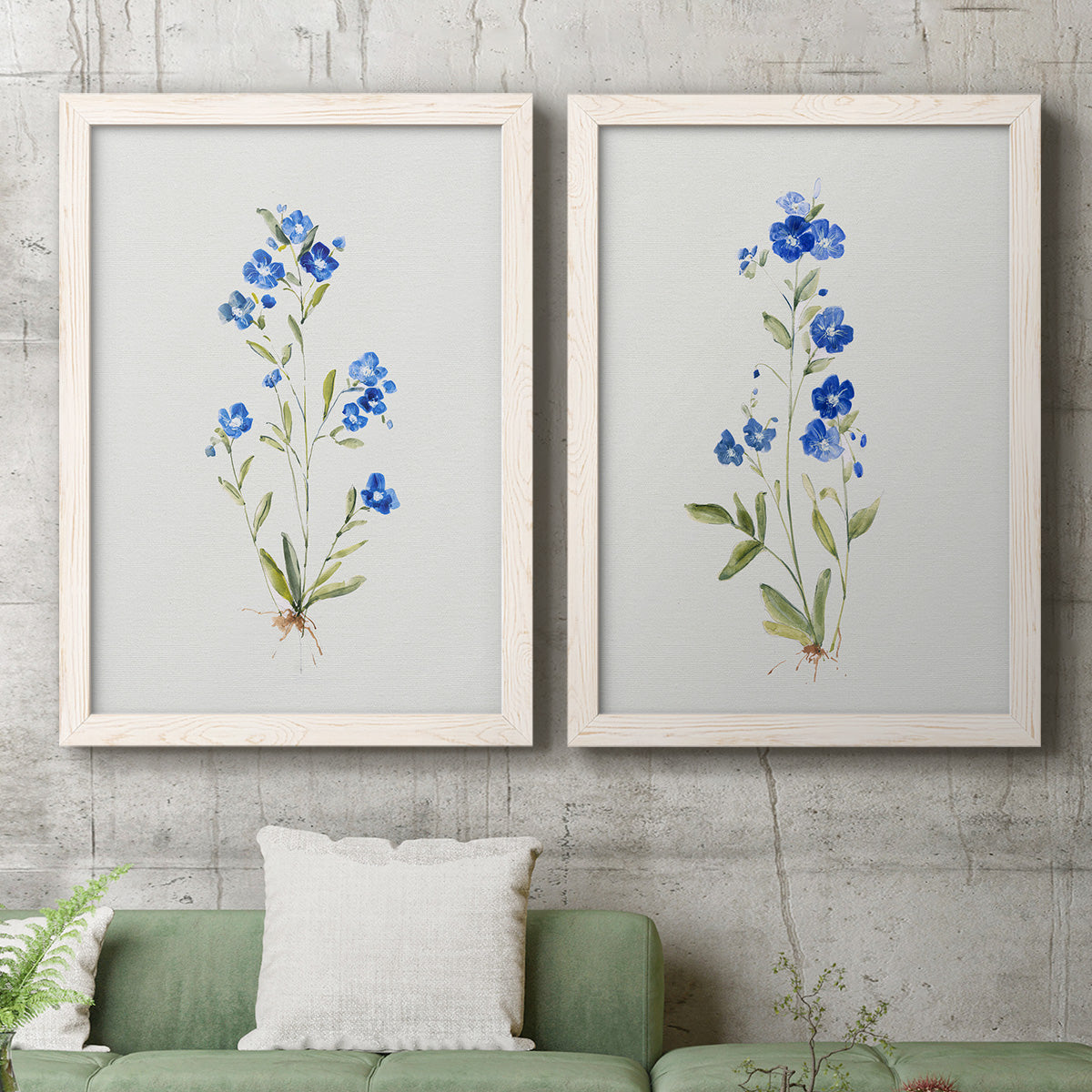 Set of two white barnwood framed canvas prints depicting a coordinated art pair of small blue wildflower stems rendered as delicate watercolor botanical studies above a sofa in a modern living room.
