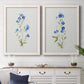 Set of two white barnwood framed canvas prints depicting a coordinated art pair of small blue wildflower stems rendered as delicate watercolor botanical studies above a dining room sideboard.