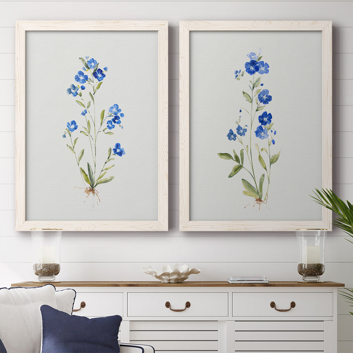 Set of two white barnwood framed canvas prints depicting a coordinated art pair of small blue wildflower stems rendered as delicate watercolor botanical studies above a dining room sideboard.