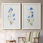 Set of two white barnwood framed canvas prints depicting two delicate watercolor botanical studies featuring small blue wildflower stems above a sideboard in a cozy sitting room.
