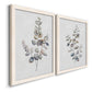 Angled view of a set of two white barnwood framed canvas prints featuring two minimalist watercolor botanical studies featuring delicate eucalyptus branches with rounded leaves.