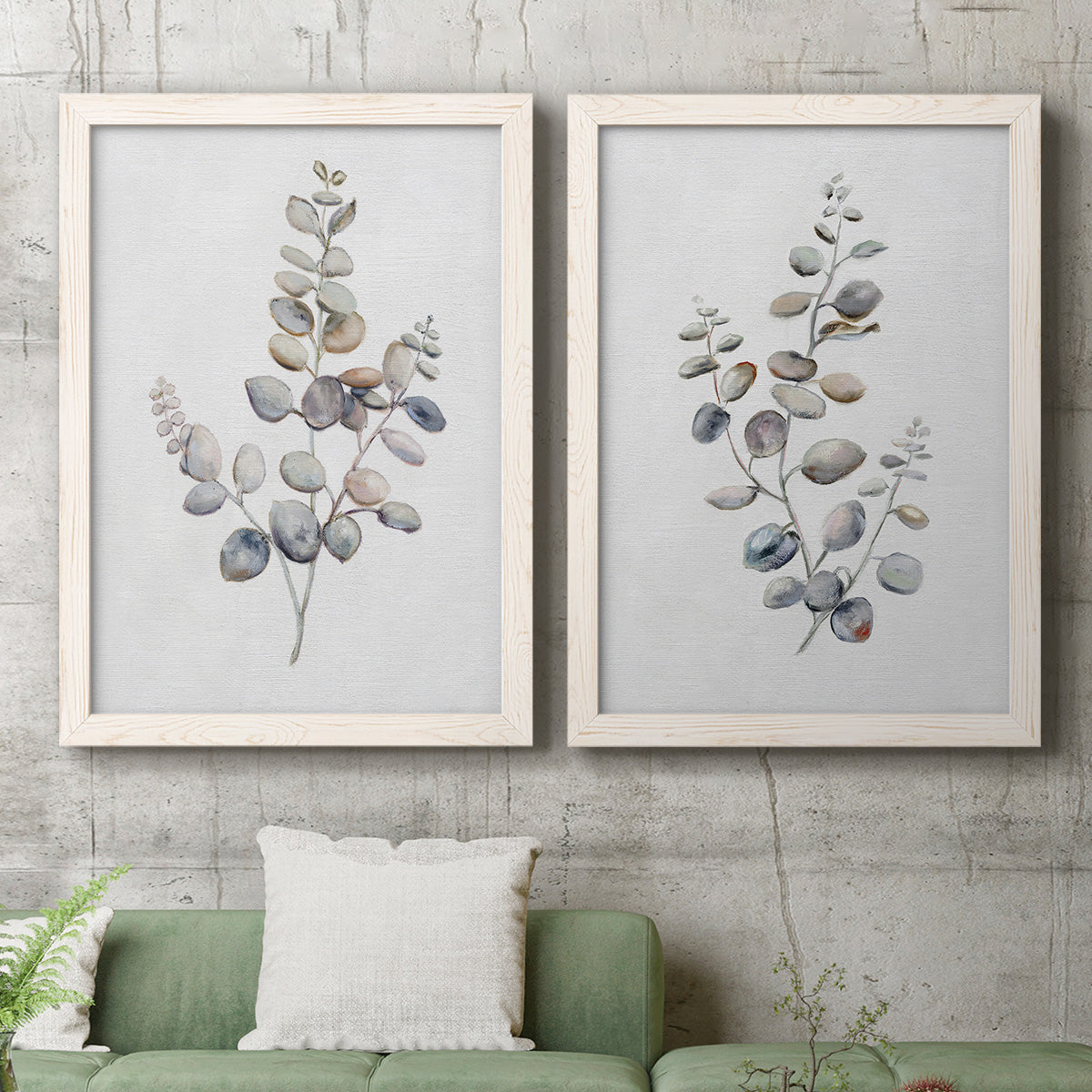 Set of two white barnwood framed canvas prints depicting a coordinated art pair of delicate eucalyptus branches with rounded leaves rendered as minimalist watercolor botanical studies above a sofa in a modern living room.