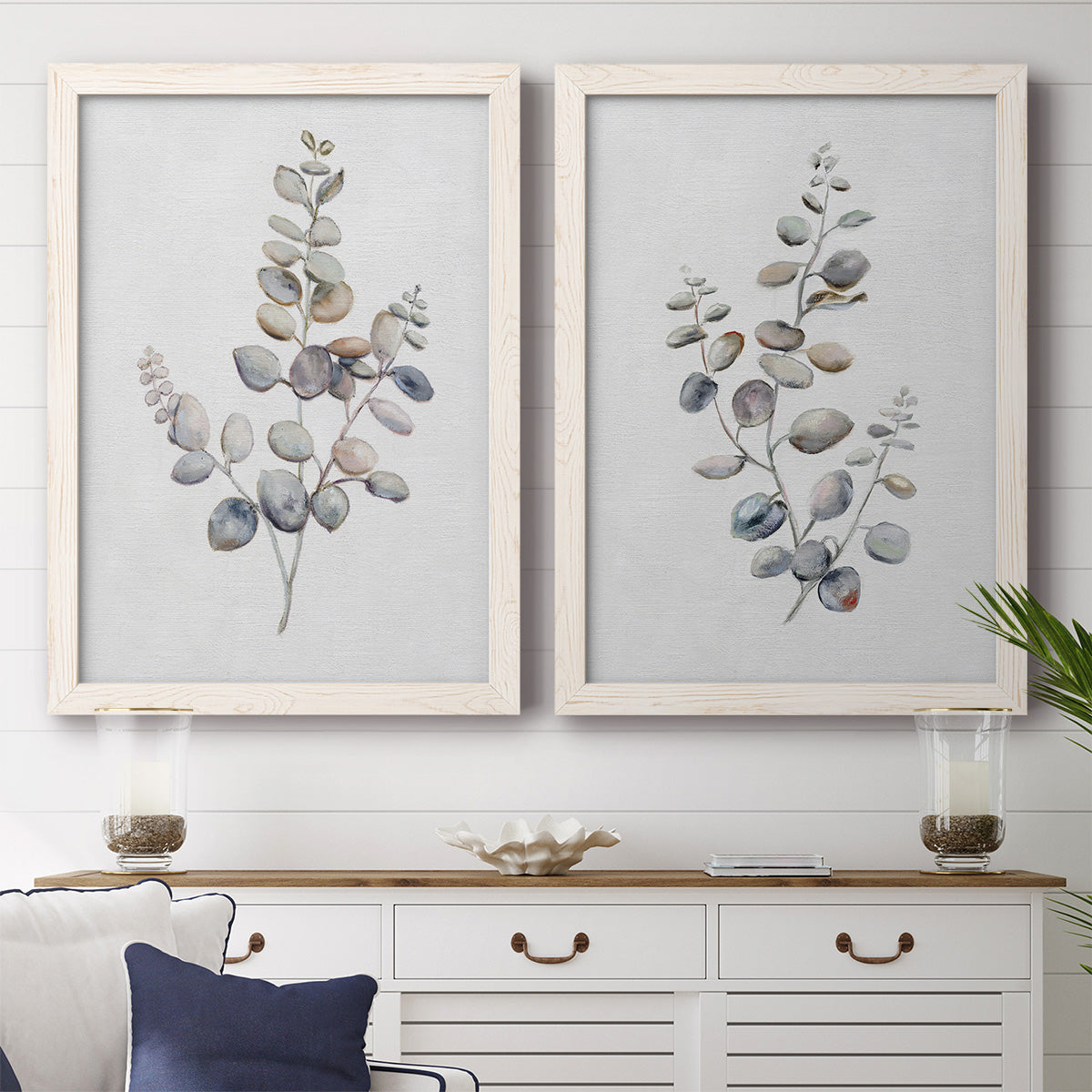 Set of two white barnwood framed canvas prints depicting a coordinated art pair of delicate eucalyptus branches with rounded leaves rendered as minimalist watercolor botanical studies above a dining room sideboard.