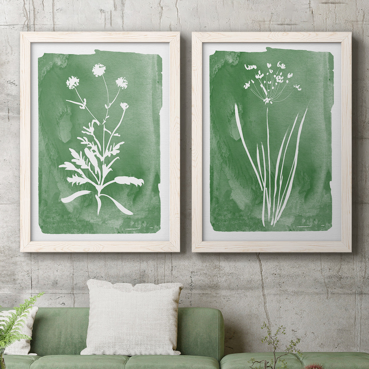 Set of two white barnwood framed canvas prints depicting a coordinated art pair of delicate wildflower and leafy stems rendered as rustic minimalist botanical studies above a sofa in a modern living room.