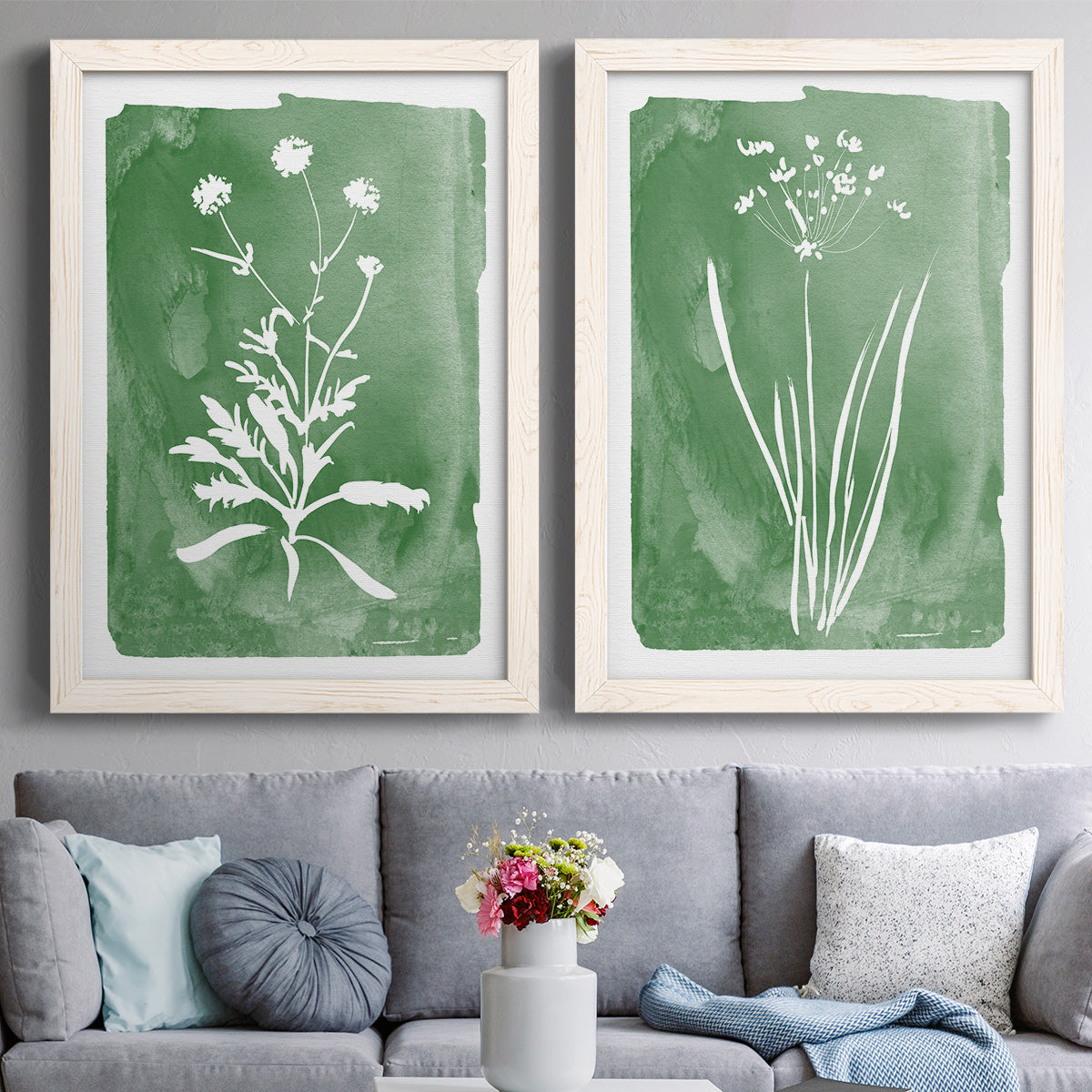 Set of two white barnwood framed canvas prints depicting paired rustic minimalist botanical studies with fine green branches, sparse blue or white blossoms, and cream grounds above a sofa in a contemporary living room.