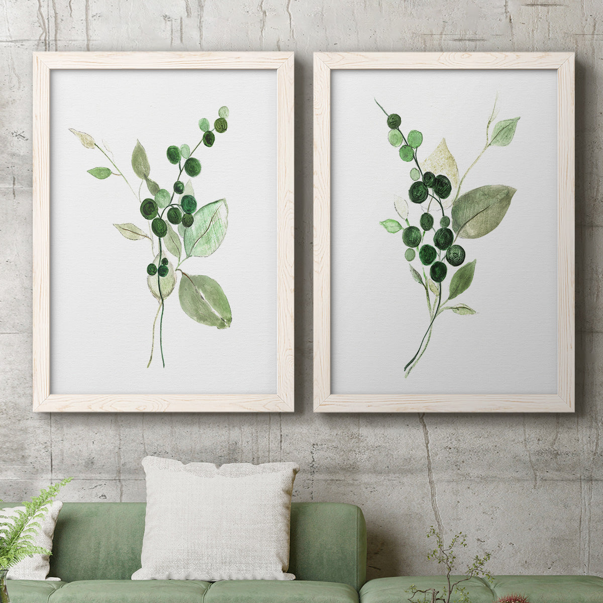 Set of two white barnwood framed canvas prints depicting a coordinated art pair of green berry sprigs and pale leaves rendered as rustic watercolor botanical studies above a sofa in a modern living room.