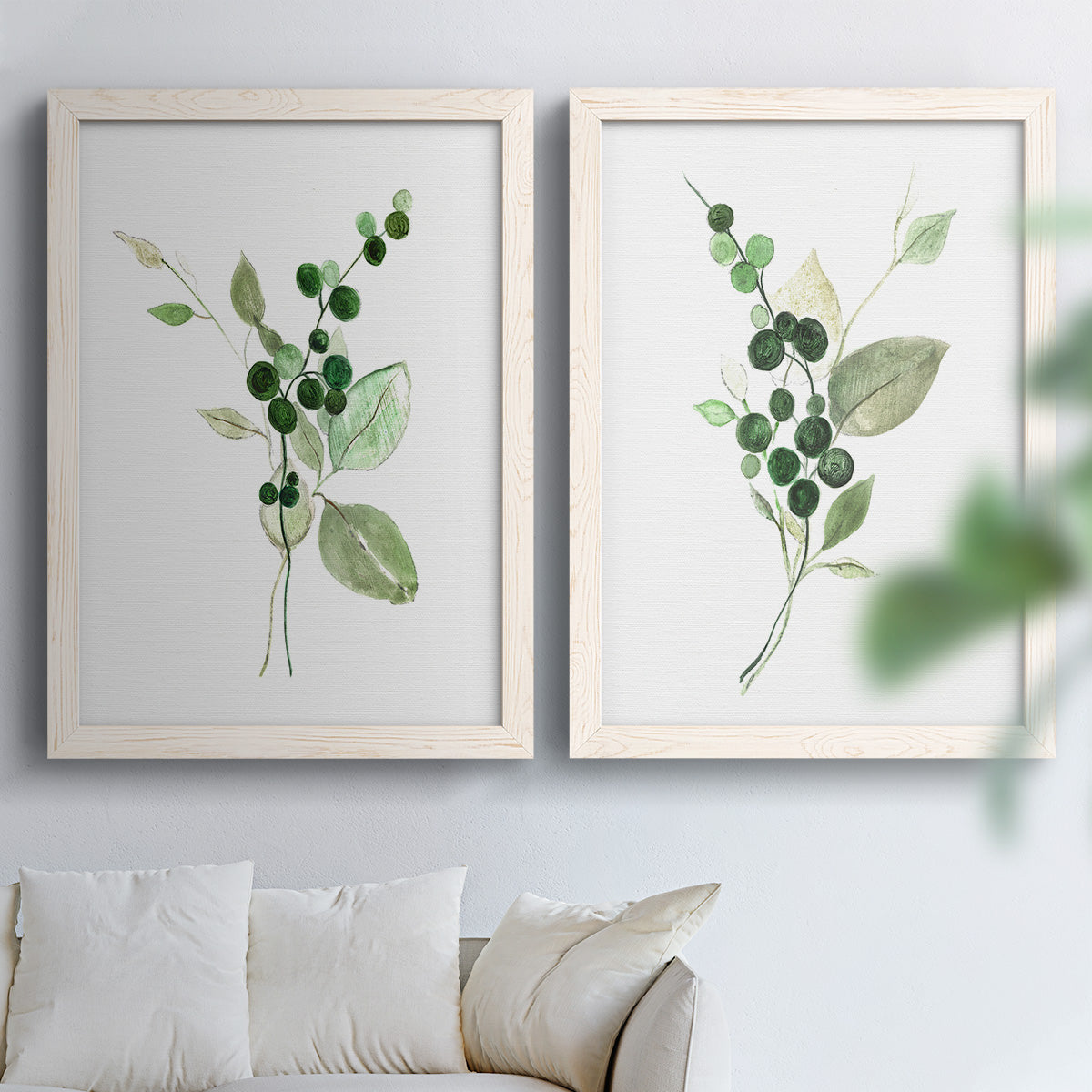 Set of two white barnwood framed canvas prints depicting dark round berries, delicate stems, and clean white space arranged across two complementary compositions above a sofa in a bright living space.