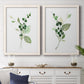Set of two white barnwood framed canvas prints depicting a coordinated art pair of green berry sprigs and pale leaves rendered as rustic watercolor botanical studies above a dining room sideboard.