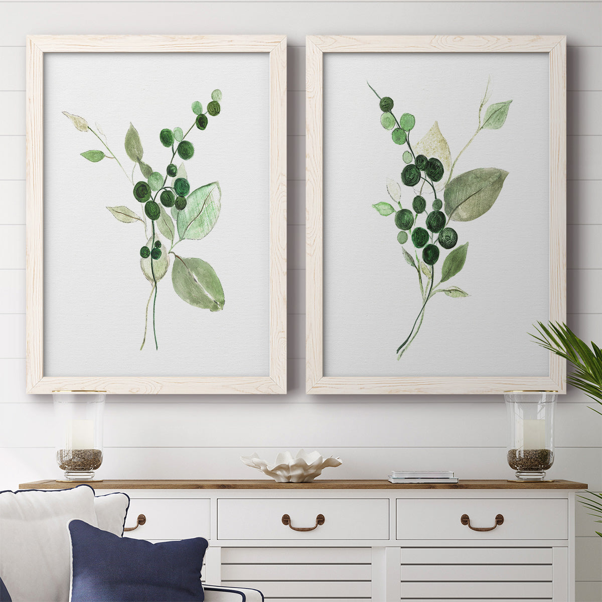 Set of two white barnwood framed canvas prints depicting a coordinated art pair of green berry sprigs and pale leaves rendered as rustic watercolor botanical studies above a dining room sideboard.