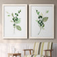 Set of two white barnwood framed canvas prints depicting two rustic watercolor botanical studies featuring green berry sprigs and pale leaves above a sideboard in a cozy sitting room.