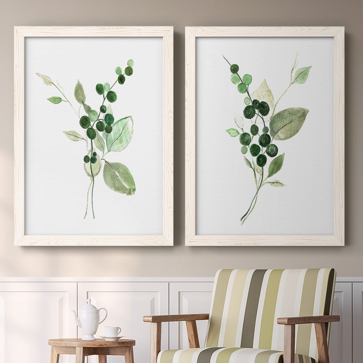 Set of two white barnwood framed canvas prints depicting two rustic watercolor botanical studies featuring green berry sprigs and pale leaves above a sideboard in a cozy sitting room.