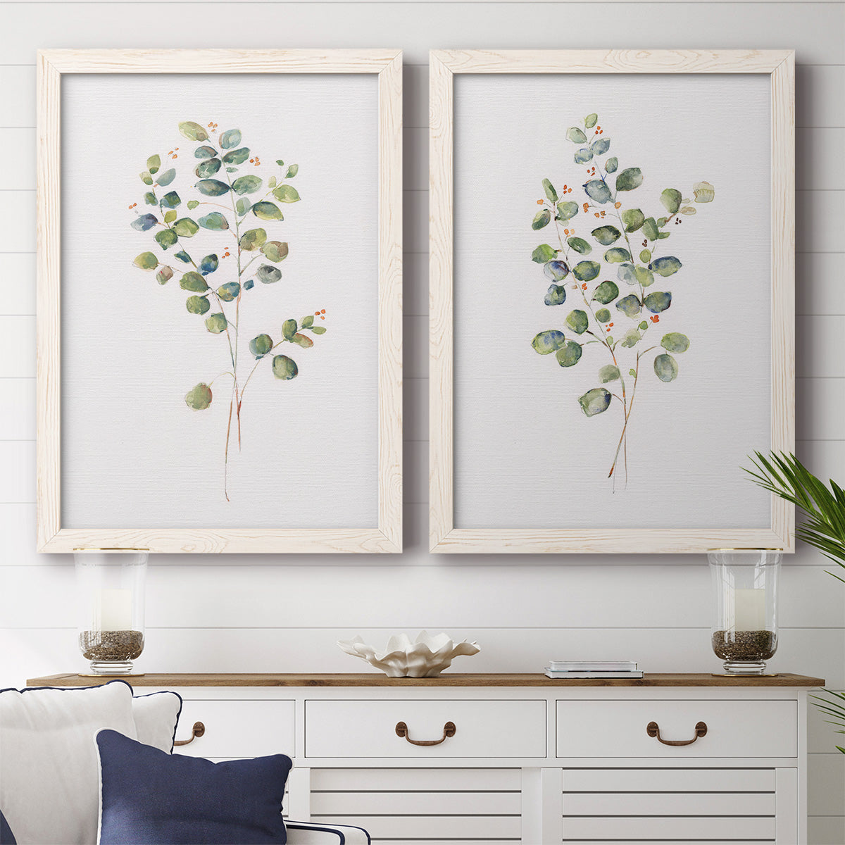 Set of two white barnwood framed canvas prints depicting a coordinated art pair of delicate eucalyptus branches with rounded leaves rendered as minimalist watercolor botanical studies above a dining room sideboard.