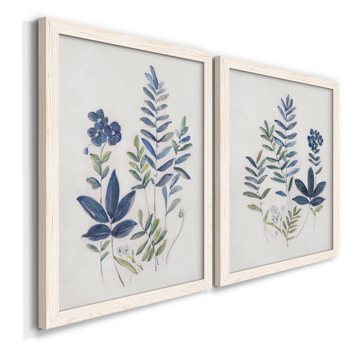 Angled view of a set of two white barnwood framed canvas prints featuring two rustic botanical illustrations featuring blue fern fronds and small woodland flowers.