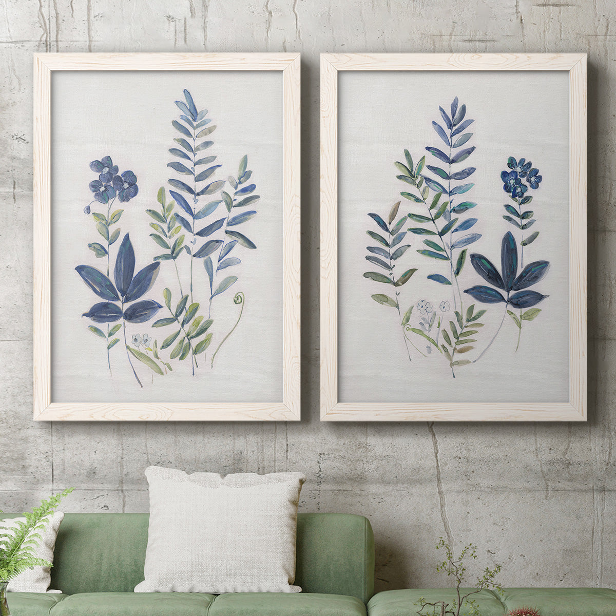 Set of two white barnwood framed canvas prints depicting a coordinated art pair of blue fern fronds and small woodland flowers rendered as rustic botanical illustrations above a sofa in a modern living room.