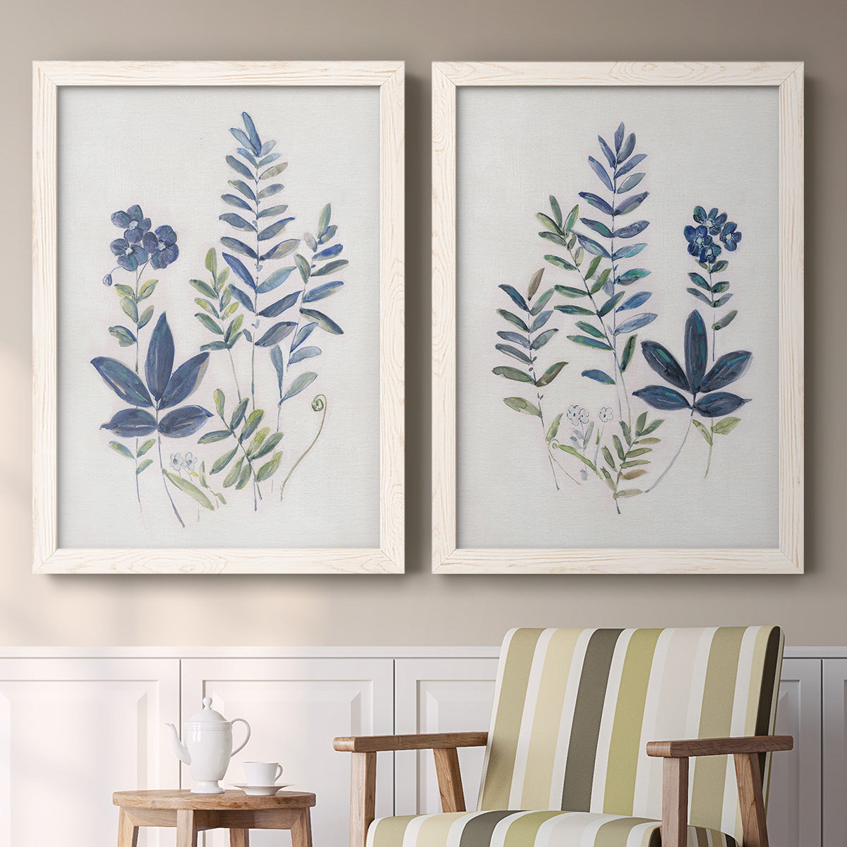 Set of two white barnwood framed canvas prints depicting two rustic botanical illustrations featuring blue fern fronds and small woodland flowers above a sideboard in a cozy sitting room.