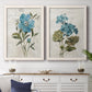 Set of two white barnwood framed canvas prints depicting a coordinated art pair of blue peony and hydrangea-like blooms over vintage script rendered as rustic floral illustrations above a dining room sideboard.
