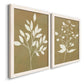 Angled view of a set of two white barnwood framed canvas prints featuring two minimalist botanical silhouettes with white leafy stems against warm honey gold backgrounds.