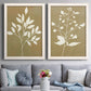 Set of two white barnwood framed canvas prints depicting coordinated foliage silhouettes in ivory tan and antique gold with clean modern spacing above a sofa in a contemporary living room.