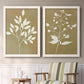 Set of two white barnwood framed canvas prints depicting two minimalist botanical silhouettes with white leafy stems against warm honey gold backgrounds above a sideboard in a cozy sitting room.