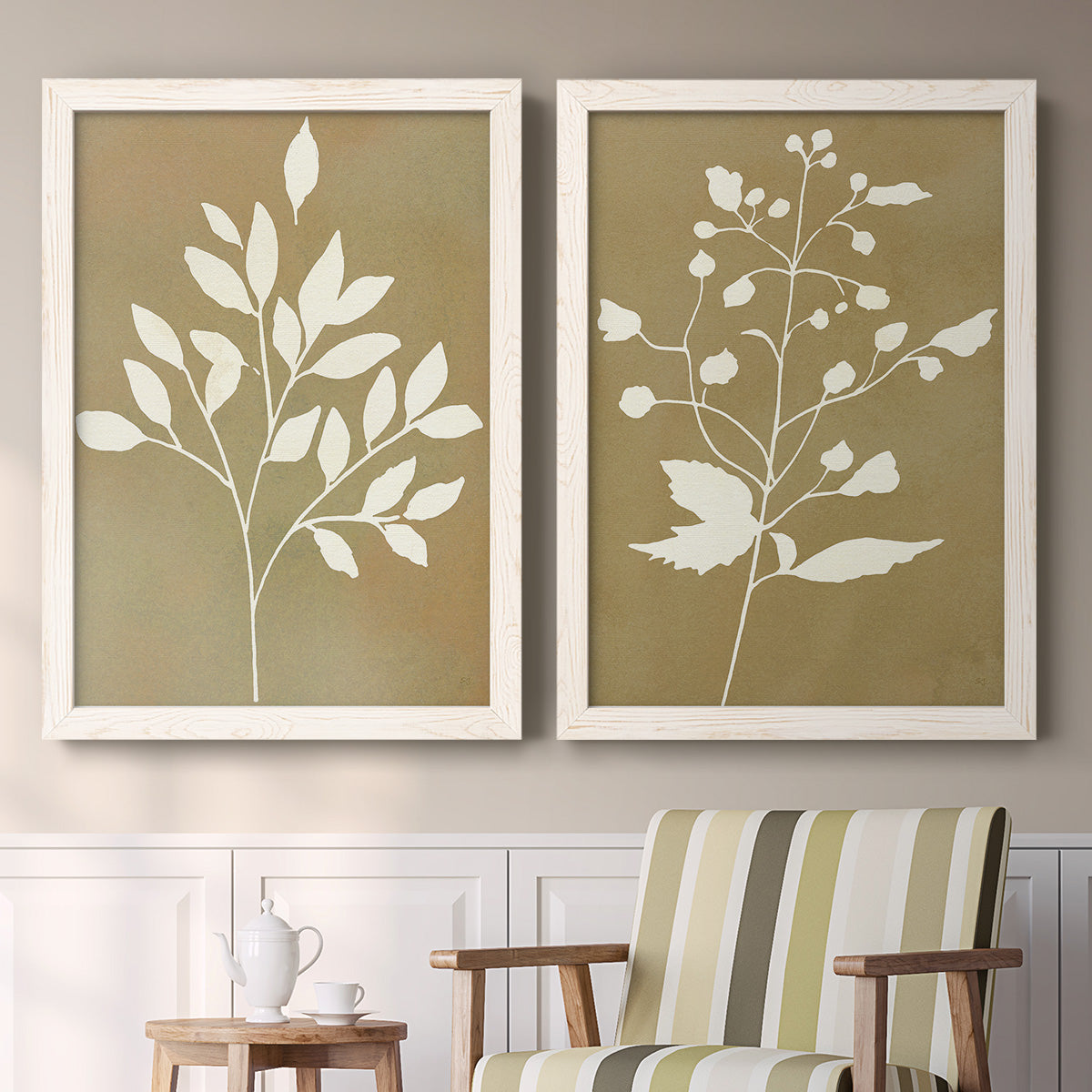 Set of two white barnwood framed canvas prints depicting two minimalist botanical silhouettes with white leafy stems against warm honey gold backgrounds above a sideboard in a cozy sitting room.