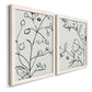 Angled view of a set of two white barnwood framed canvas prints featuring two minimalist botanical line art featuring black contour drawings of leaves and flowers.