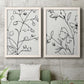 Set of two white barnwood framed canvas prints depicting a coordinated art pair of black contour drawings of leaves and flowers rendered as minimalist botanical line art above a sofa in a modern living room.