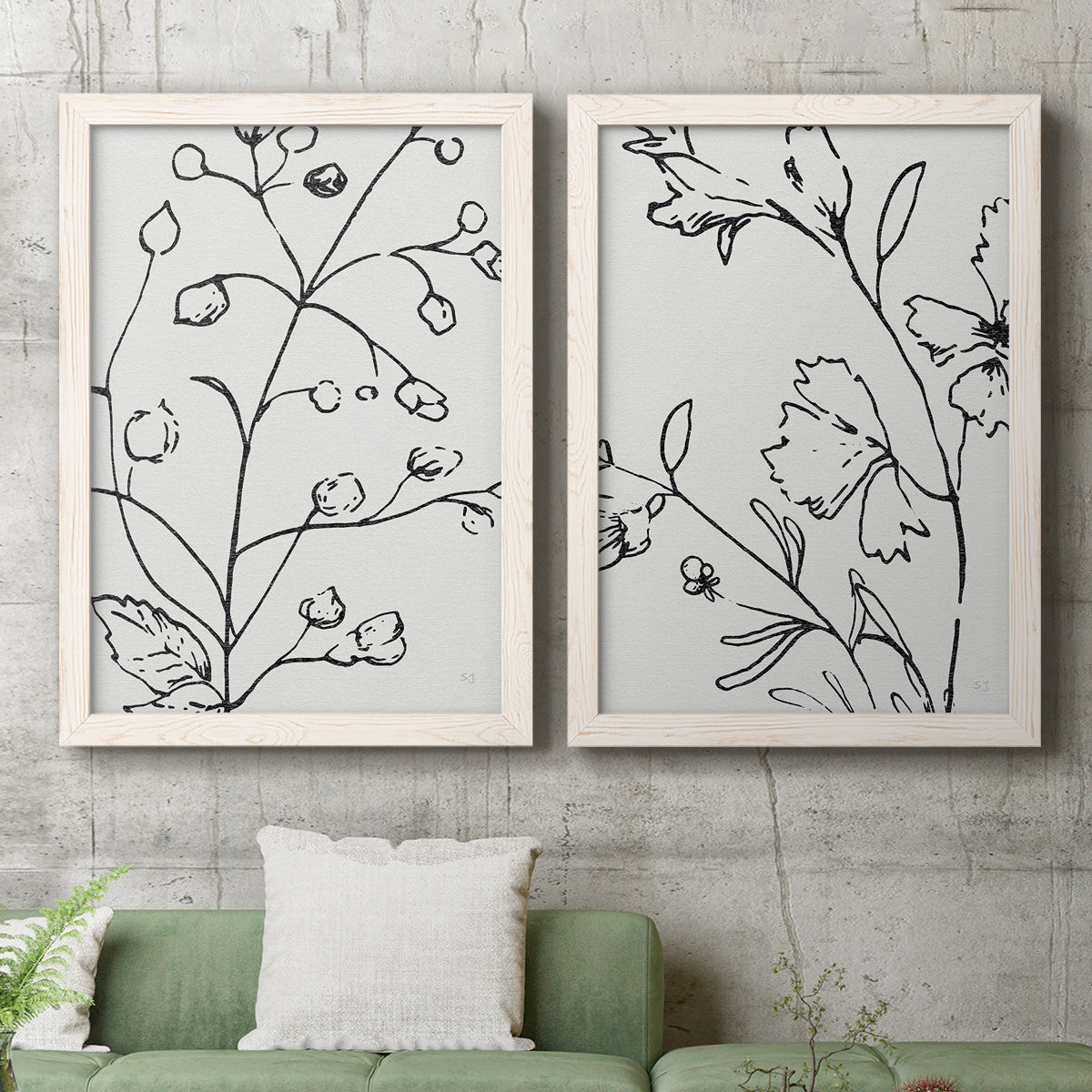 Set of two white barnwood framed canvas prints depicting a coordinated art pair of black contour drawings of leaves and flowers rendered as minimalist botanical line art above a sofa in a modern living room.