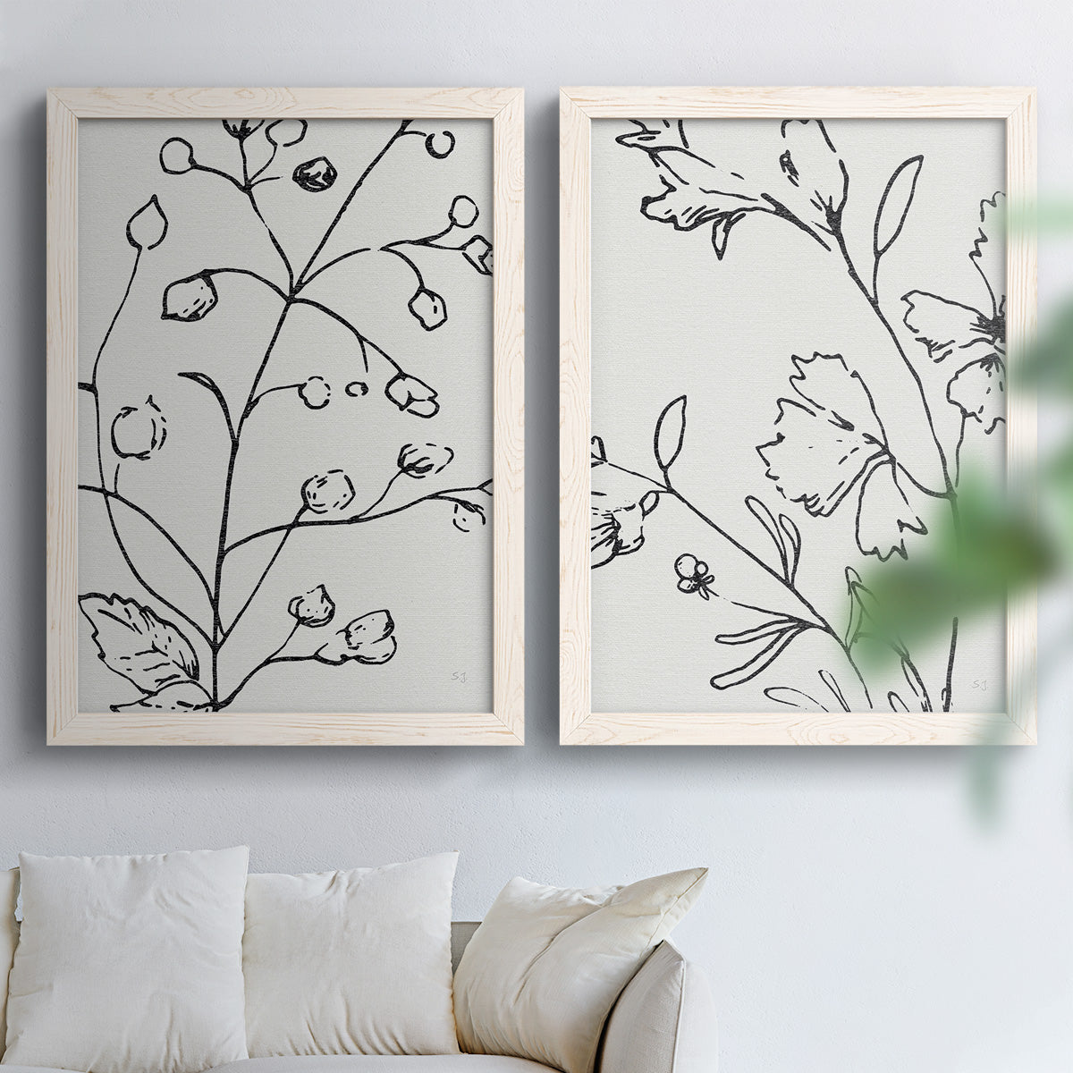 Set of two white barnwood framed canvas prints depicting fine monochrome outlines, cropped stems, and clean white fields arranged across two complementary compositions above a sofa in a bright living space.