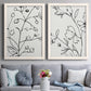 Set of two white barnwood framed canvas prints depicting paired minimalist botanical line art with fine monochrome outlines, cropped stems, and clean white fields above a sofa in a contemporary living room.