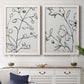 Set of two white barnwood framed canvas prints depicting a coordinated art pair of black contour drawings of leaves and flowers rendered as minimalist botanical line art above a dining room sideboard.