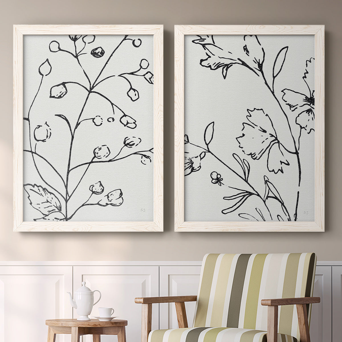 Set of two white barnwood framed canvas prints depicting two minimalist botanical line art featuring black contour drawings of leaves and flowers above a sideboard in a cozy sitting room.