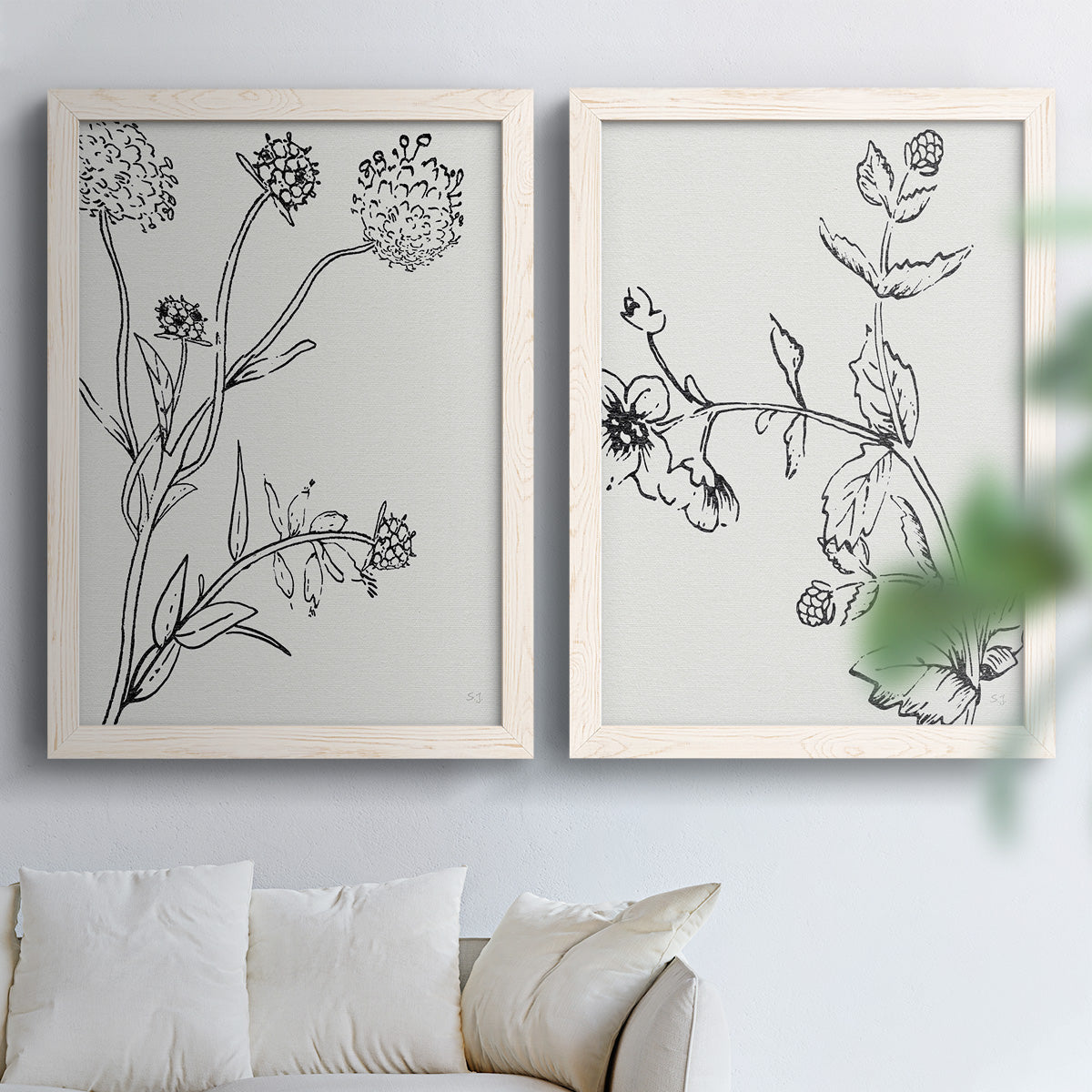 Set of two white barnwood framed canvas prints depicting fine stems, seed heads, blossoms, and open white backgrounds arranged across two complementary compositions above a sofa in a bright living space.