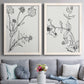Set of two white barnwood framed canvas prints depicting paired minimalist botanical sketches with fine stems, seed heads, blossoms, and open white backgrounds above a sofa in a contemporary living room.