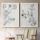 Set of two white barnwood framed canvas prints depicting two minimalist botanical sketches featuring black line drawings of wildflowers and leaves above a sideboard in a cozy sitting room.
