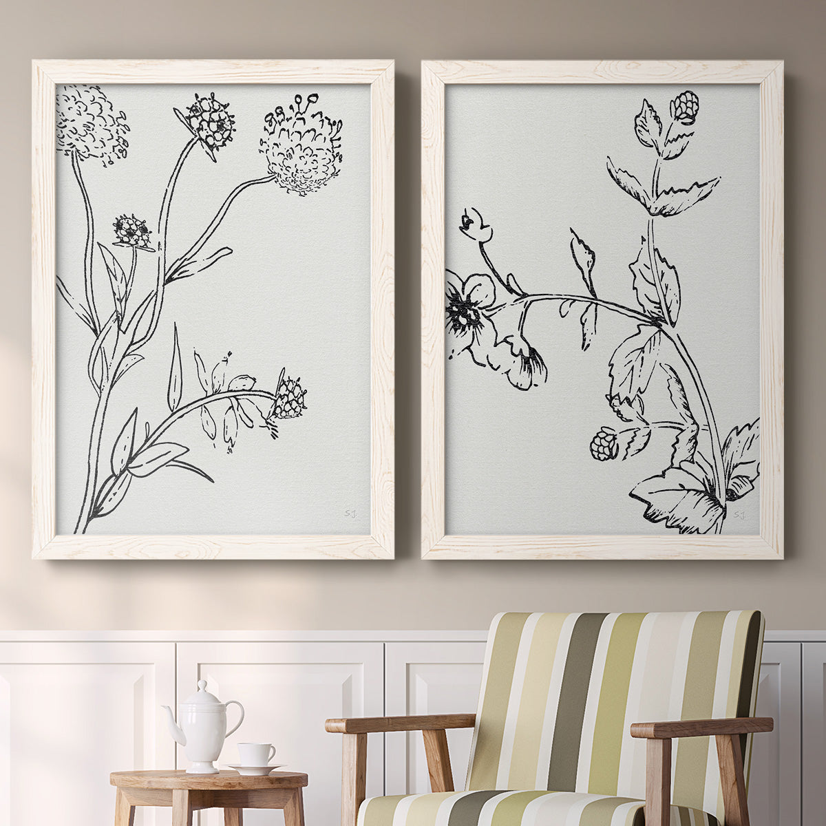 Set of two white barnwood framed canvas prints depicting two minimalist botanical sketches featuring black line drawings of wildflowers and leaves above a sideboard in a cozy sitting room.