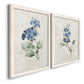 Angled view of a set of two white barnwood framed canvas prints featuring two farmhouse botanical illustrations featuring blue periwinkle flowers with leafy stems.